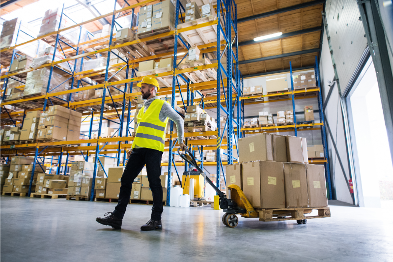 Warehouse worker pulling pallet jack with boxes